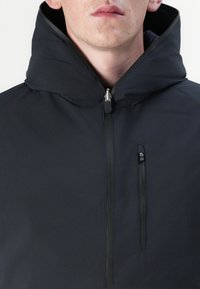 Schwarze Kapuzenjacke aus glattem Stoff. Verfügt über einen Reißverschluss vorne und eine Reißverschlusstasche auf der linken Brust. Minimalistisches Design.