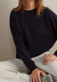 Mörkblå stickad tröja med en ribbad halsringning och långa ärmar, kombinerad med ljusgrå avslappnade byxor med mjuk textur.