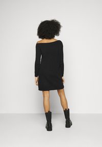 Černé pletené šaty bez ramínek s dlouhými rukávy a rovnými liniemi, doplněné o robustní černé boty. Matná textura, ležérní styl.