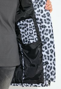 Giacca isolante con fodera a stampa leopardo bianca e nera, esterno lucido nero, bottoni a pressione e tasca interna.
