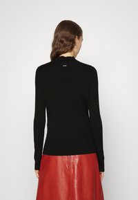 Czarny prążkowany sweter z długim rękawem, okrągłym dekoltem i subtelnym logo z tyłu, zestawiony z czerwoną skórzaną spódnicą.