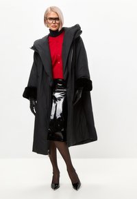 Sort polstret frakke med bred hætte og kunstpelsmanchetter, lagdelt over en rød knap-op skjorte og skinnende sort blyantskjørt, tilbehør med handsker.