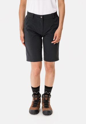 Schwarze Shorts aus leichtem Material, knielang mit vorderen Taschen, mit glatter Textur und elastischem Bund. Braune Wanderschuhe und gemusterte Socken.