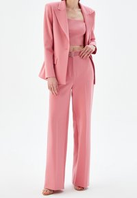 Woman wearing a coordinated pink suit with wide-leg pants, belted waist, cropped top, and matching blazer with open-toe heels.