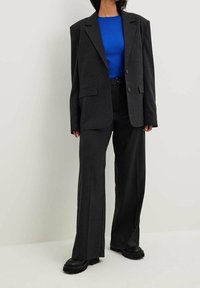 Osoba ubrana w ciemnoszary, oversize'owy blezer i szerokie spodnie z jasnoniebieskim, prążkowanym topem oraz czarne, masywne buty.