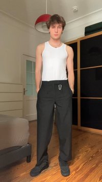 Un débardeur blanc, un pantalon large noir avec des passants de ceinture, et des baskets noires, dans une pièce avec un sol en bois et un mobilier minimaliste.