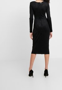 Schwarzes, langärmeliges Midikleid aus einem weichen, strukturierten Stoff. Hat eine figurbetonte Silhouette und einen Rückenschlitz, sowie einen dezenten Schlitz am Saum.