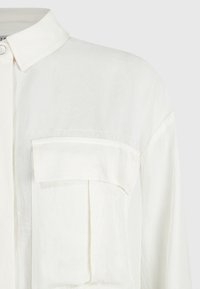 Vit skjorta med krage och knappstängning. Har en bröstficka, avslappnad passform och texturerad tyg.