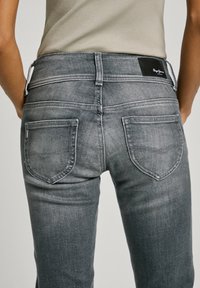 Šedé denimové džíny s fitted designem, které mají dvě zadní kapsy, detaily šití a černou koženou nášivku na pase.