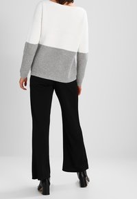 Dzianinowy sweter z białym i szarym blokiem kolorów, prążkowaną fakturą oraz szerokim, łodziowym dekoltem. Połączony z czarnymi, rozszerzanymi spodniami i botkami za kostkę.