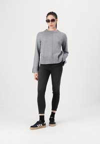 Grijze gebreide trui met geribde zoom en manchetten, gecombineerd met zwarte skinny jeans en zwarte sneakers met witte strepen.