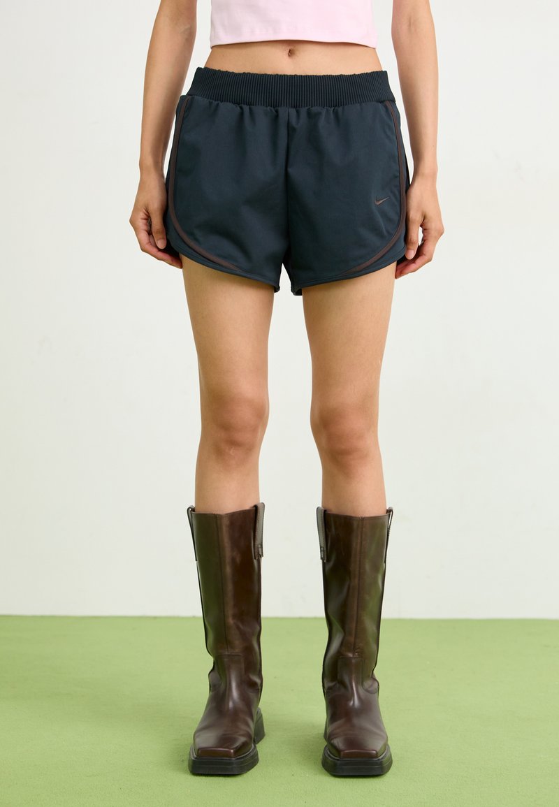Navy running shorts with a ribbed waistband and contrast trim, paired with knee-high brown leather boots. Flat textured surface.