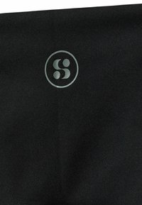 Črna tkanina z okroglo oznako v svetlo sivi barvi, s stiliziranim simbolom "S". Tekstura se zdi gladka in rahlo odsevna.