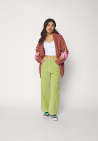 Cardigan marrón de punto con bordado floral rosa, top corto blanco con fruncidos, pantalones de pana verde de pierna ancha y zapatillas rosa-verde.