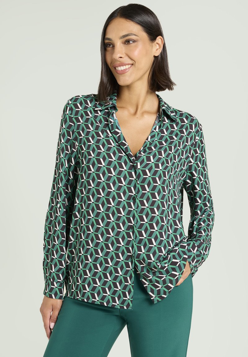 Zielona i czarna bluzka w geometryczne wzory, z długimi rękawami, zapinana na guziki z przodu, wykonana z lekkiego materiału.