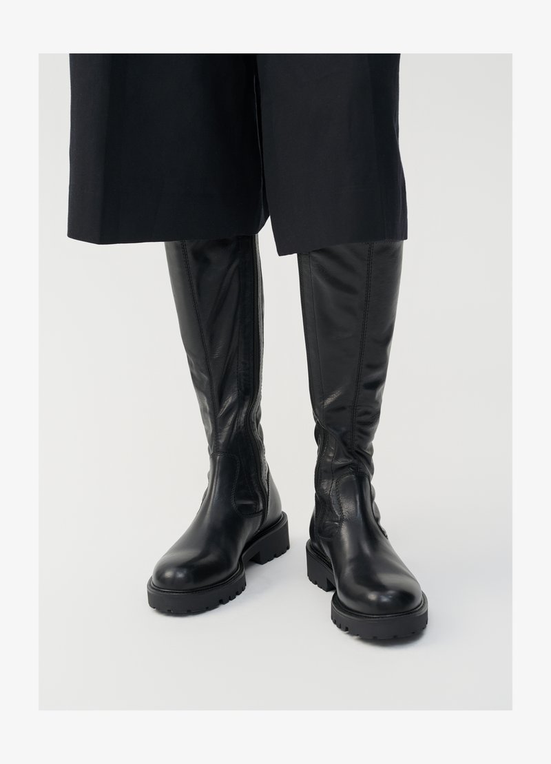 Stivali neri in pelle al ginocchio con una texture liscia, suole spesse e cerniere laterali. Il design presenta una sottile lavorazione delle cuciture.