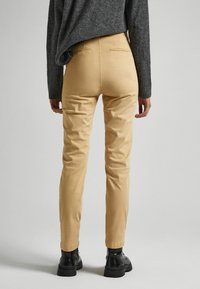 Khaki úzké kalhoty vyrobené z bavlny s zadními kapsami, nošené s šedým svetrem a černými kotníkovými botami. Hladká textura a přiléhavý design.