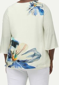 Top bianco con maniche a tre quarti, caratterizzato da grandi motivi floreali blu e viola sulla schiena, texture liscia e scollatura arrotondata.