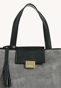 Sac en cuir noir avec un corps en suédine grise, présentant un accent en métal doré et un détail à frange sur le côté.