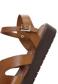 Sandale en cuir marron avec bride réglable à boucle et semelle épaisse noire texturée, inclinée pour montrer les détails latéraux et avant.