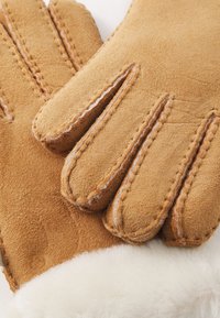 Kavos suede pirštinės su baltu vilnos pamušalu, turinčios keturių dalių pirštų dizainą ir matomomis siūlėmis. Minkšta tekstūra ir patvari medžiaga.