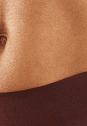 Nahaufnahme des Mittelbereichs einer Person mit glatter brauner Haut, einem Bauchnabel und dem Bund dunkler brauner Kleidung.