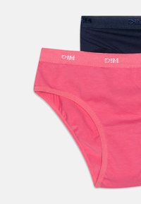 Deux paires de culottes en coton : une rose avec une ceinture texturée, une bleue marine avec une ceinture lisse, toutes deux présentant des détails de logo.