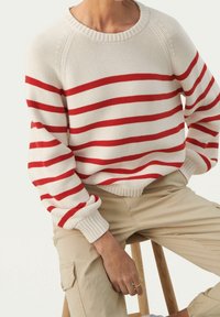 Czerwono-biały sweter z paskami, wykonany z dzianiny, z okrągłym dekoltem i prążkowanymi mankietami. Wykonany z lekkej, teksturowanej tkaniny o luźnym kroju.