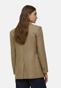 Blazer a quadri marrone con vestibilità su misura, caratterizzato da un revers a notch, polsini con due bottoni e una texture liscia.