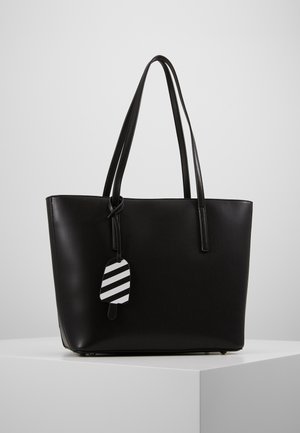 Schwarze Ledertasche mit zwei Griffen und einem schwarz-weiß gestreiften, eisförmigen Anhänger, der an einem Griff hängt.