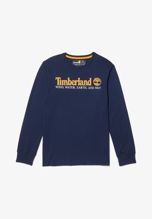 Camisa de manga larga azul marino con el logo de "Timberland" y símbolo de árbol en amarillo, y texto "VIENTO, AGUA, TIERRA Y CIELO" en blanco a lo largo del pecho.