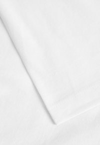 Gros plan d'une surface en tissu de coton blanc montrant une couture précise le long du bord plié.
