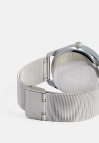 Orologio in acciaio inossidabile con cinturino a rete, finitura argentata lucida e cassa tonda. Chiusura visibile e dettagli posteriori, inclusi i marchi di certificazione.