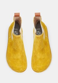 Botas de tobillo de ante amarillo con una textura suave, paneles laterales elásticos y una lengüeta de cuero marrón en la parte posterior. Suela plana de tono natural.