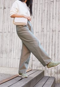 Una modella indossa un maglione lavorato a maglia color crema e pantaloni verdi oliva a vita alta, abbinati a sneaker verde menta e porta una borsa a tracolla intrecciata color crema.