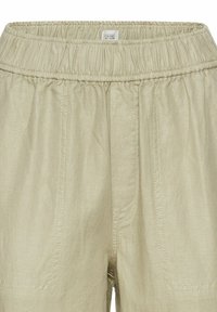 Lys beige, lette bukser med elastisk talje, som har to frontlommer og synlige syninger på stoffet.