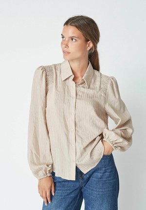 Light beige button-up shirt with vertical stripes, smocked shoulder detailing, and long, puffed sleeves. Worn with blue denim jeans.