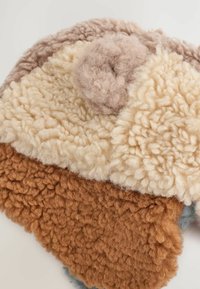 Textured wool patchwork featuring beige, brown, and soft gray tones with a prominent fluffy accent in the center.