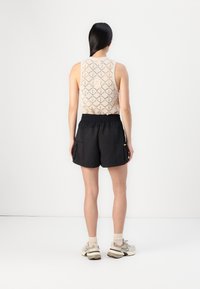 Beige pletený top bez rukávů s diamantovým vzorem, spárovaný s černými šortkami s bočními kapsami a elastickým pasem, obutý s lehkými teniskami.