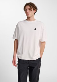 Vit kortärmad t-shirt i bomull, med en svart chevron-logotyp på vänster bröst och en avslappnad passform. Matchad med svarta byxor.