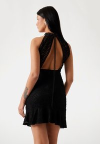 Black dress featuring a crochet design with an open back, halter neck, and ruffled hem, highlighting textured material and intricate patterns.