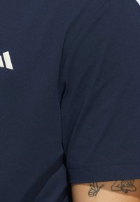 Granatowa koszulka sportowa z gładkiego, lekkiego materiału; z krótkimi rękawami i białym logiem na piersi.