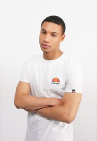 Weißes Baumwoll-T-Shirt mit kurzen Ärmeln, runden Ausschnitt und einem bunten Logo auf der Brust. Texturiert und mit klassischer Passform.