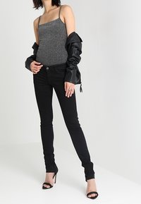Top gris de tirantes, chaqueta de cuero negra, jeans ajustados negros y tacones de punta abierta negros. Textura suave y diseño ajustado.