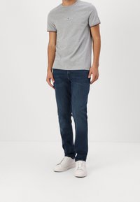 Harmaa puuvillapaita, jossa on lyhyet hihat ja punaisia sekä tummansinisiä raidallisia yksityiskohtia. Yhdistetty tummansinsisiin farkkuihin ja valkoisiin tennareihin.