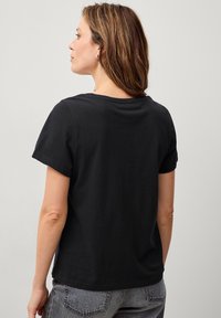 Schwarzes Kurzarm-T-Shirt aus weichem Baumwollmaterial. Crew-Neck-Design mit lockerer Passform, das eine glatte Textur und einen schlichten Rücken aufweist.