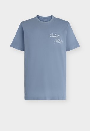 Μπλε κοντομάνικη μπλούζα με στρογγυλή λαιμόκοψη και λευκό λογότυπο "Calvin Klein" με καλλιγραφικά γράμματα στο πάνω αριστερό μέρος του στήθους.
