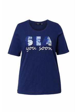 Marineblaues T-Shirt mit Rundhalsausschnitt und kurzen Ärmeln, mit dem Schriftzug "SEA" in gemusterten Blockbuchstaben und darunter "you soon" in weißer Schreibschrift.
