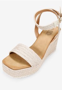 Sandale compensée avec tige en beige tissé, large bride sur le devant, bride de cheville ajustable et semelle plateforme texturée.