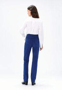 Blauwe high-waisted broek van een gladde stof, met twee achterzakken en een recht gesneden ontwerp, gecombineerd met een witte blouse met lange mouwen.